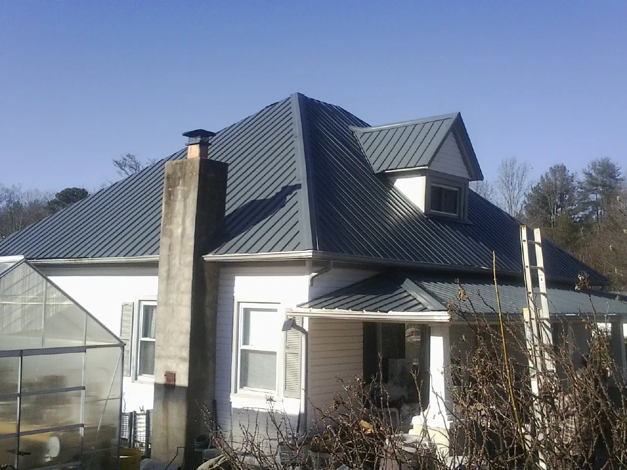 Dark blue standing seam metal roof on a white farmhouse with dormer — Slate & Tile Roof Repair by Roofing Brothers in Troutman