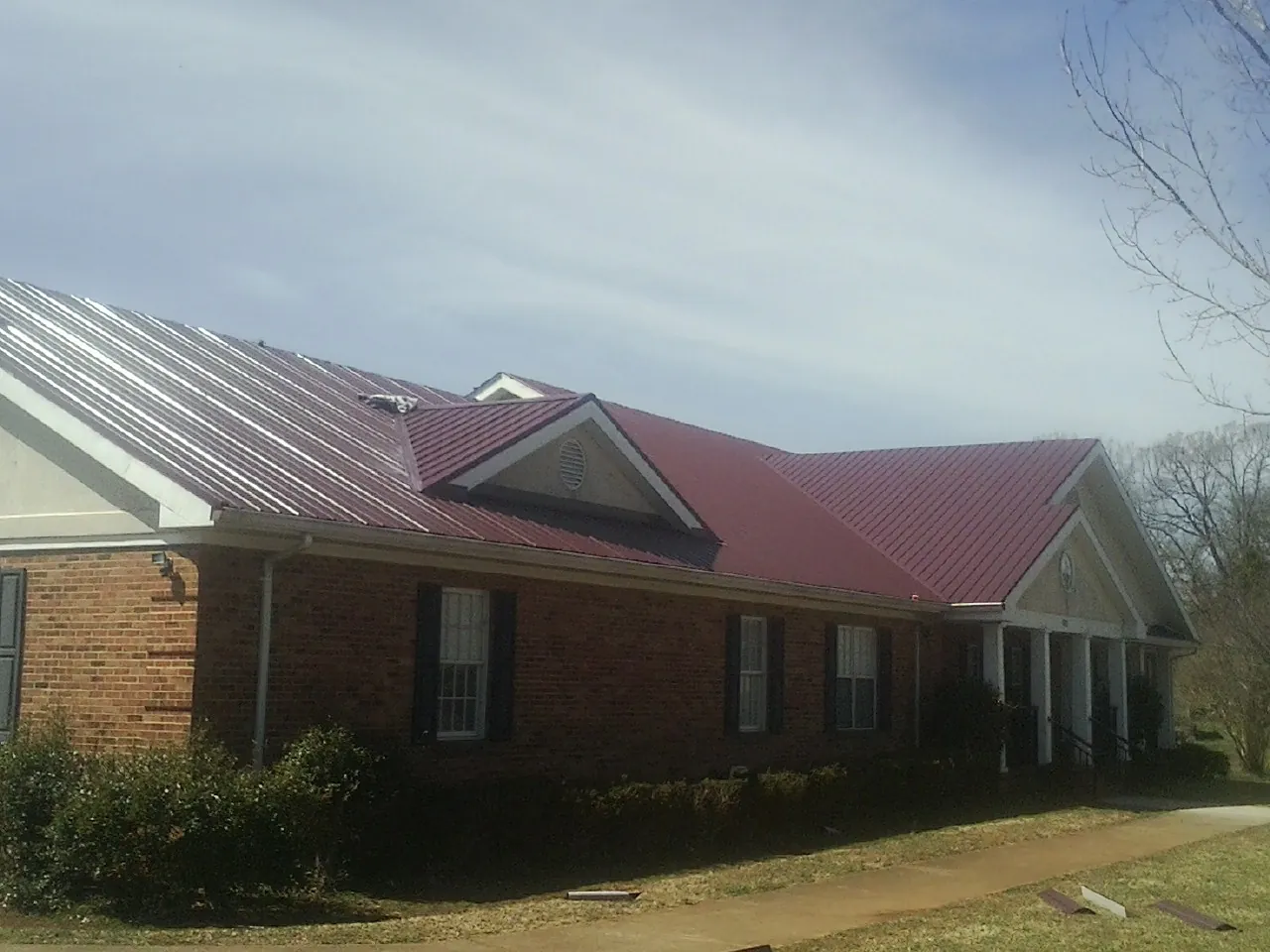Red metal roof with gabled entries on a long brick building, from a Hail Damage Roof Repair job in Troutman
