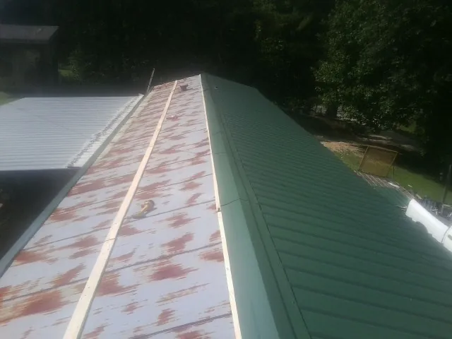 Old rusted panels beside newly installed green metal roofing — Wind Damage Roof Repair by Roofing Brothers in Troutman