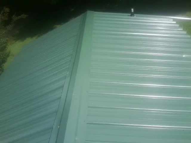 New green metal panels meeting at the ridge of a roof — Flat Roof Repair work by our crew in Troutman