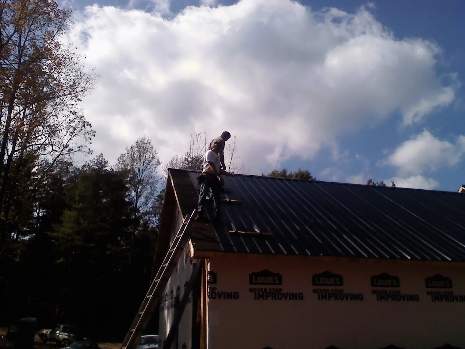 Roofer fastening dark metal panels high against a cloudy sky, from a Roof Inspection job in Troutman